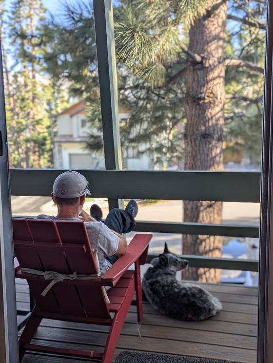 Jerry relaxing in a red Adirondack chair on a deck, his dog lying beside him